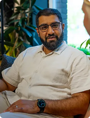 Man in a beige shirt during a business advisory services conversation, seated by a window with plants.