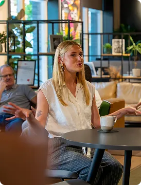 Woman speaking during a business consultancy meeting at a café table with colleagues in the background.