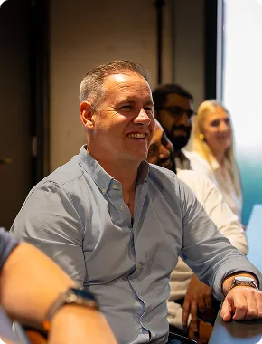 Man smiling in the audience at a business finance seminar, with colleagues seated behind him.